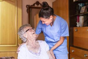 Glückliche Seniorin lachend mit ihrem Betreuer zu Hause. Konzept der häuslichen Pflege für Senioren.