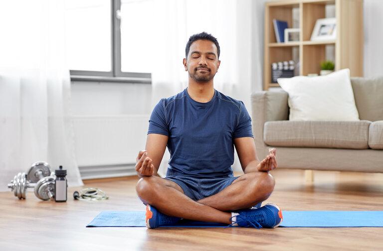 Fitness, Meditation und gesunder Lebensstil - Mann meditiert in Lotus-Pose auf einer Übungsmatte zuhause.