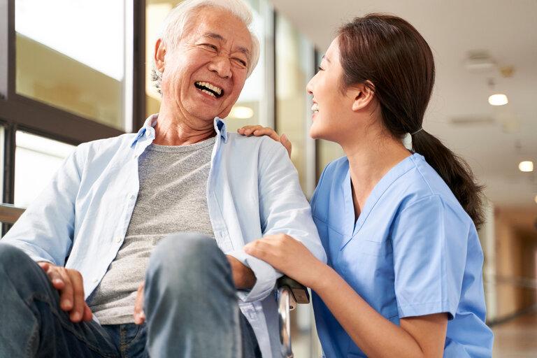 Junge freundliche asiatische Pflegerin im Gespräch mit einem älteren Mann