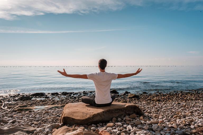 Junger Mann übt Yoga-Meditation und Atemarbeit im Freien am Meer
