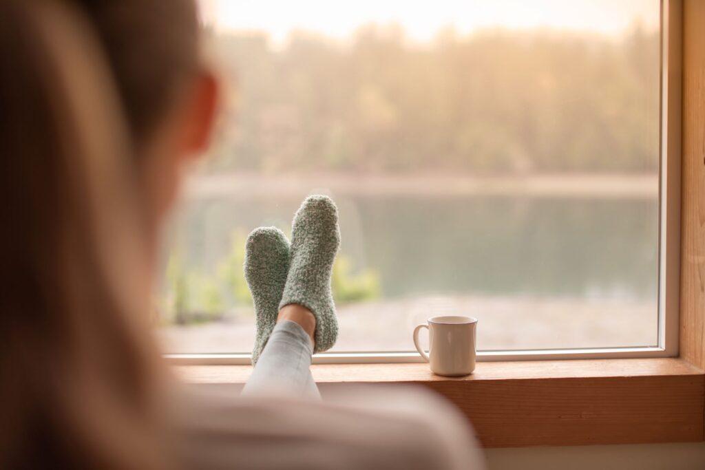 Person entspannt sich mit warmen Socken und einer Tasse Tee am Fenster, unterstützt durch Akustikpaneele aus Eiche zur Geräuschreduzierung