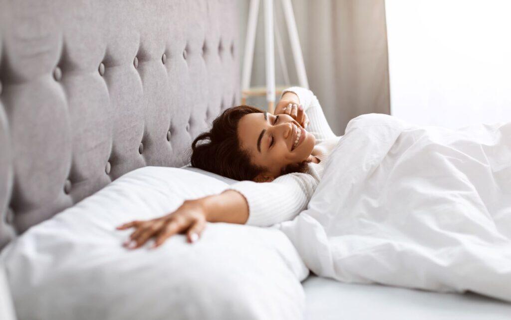 Eine glückliche Frau streckt sich morgens zufrieden in ihrem Boxspringbett und genießt den erholsamen Schlafkomfort.