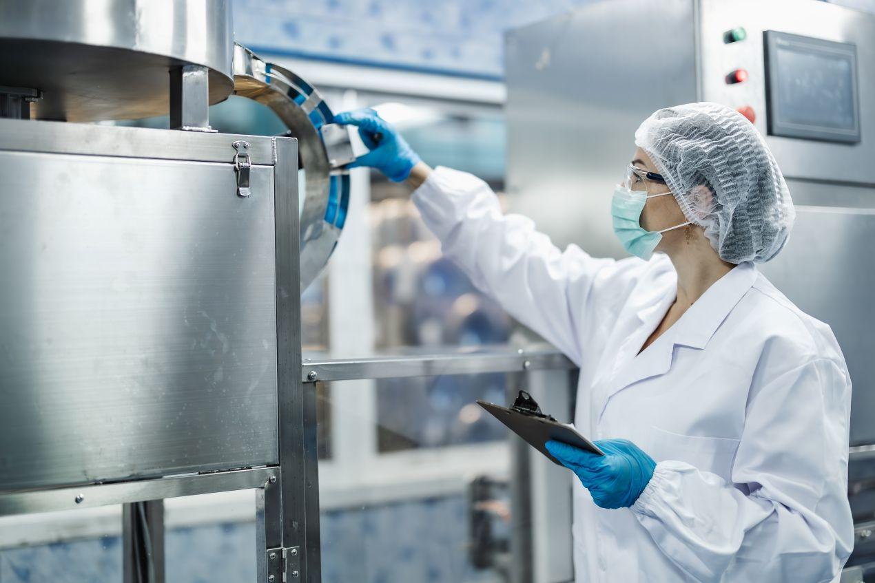 E-Learning Hygiene: Fachkraft mit Schutzkleidung und Tablet uebersieht Hygieneprozesse in Produktionsumgebung