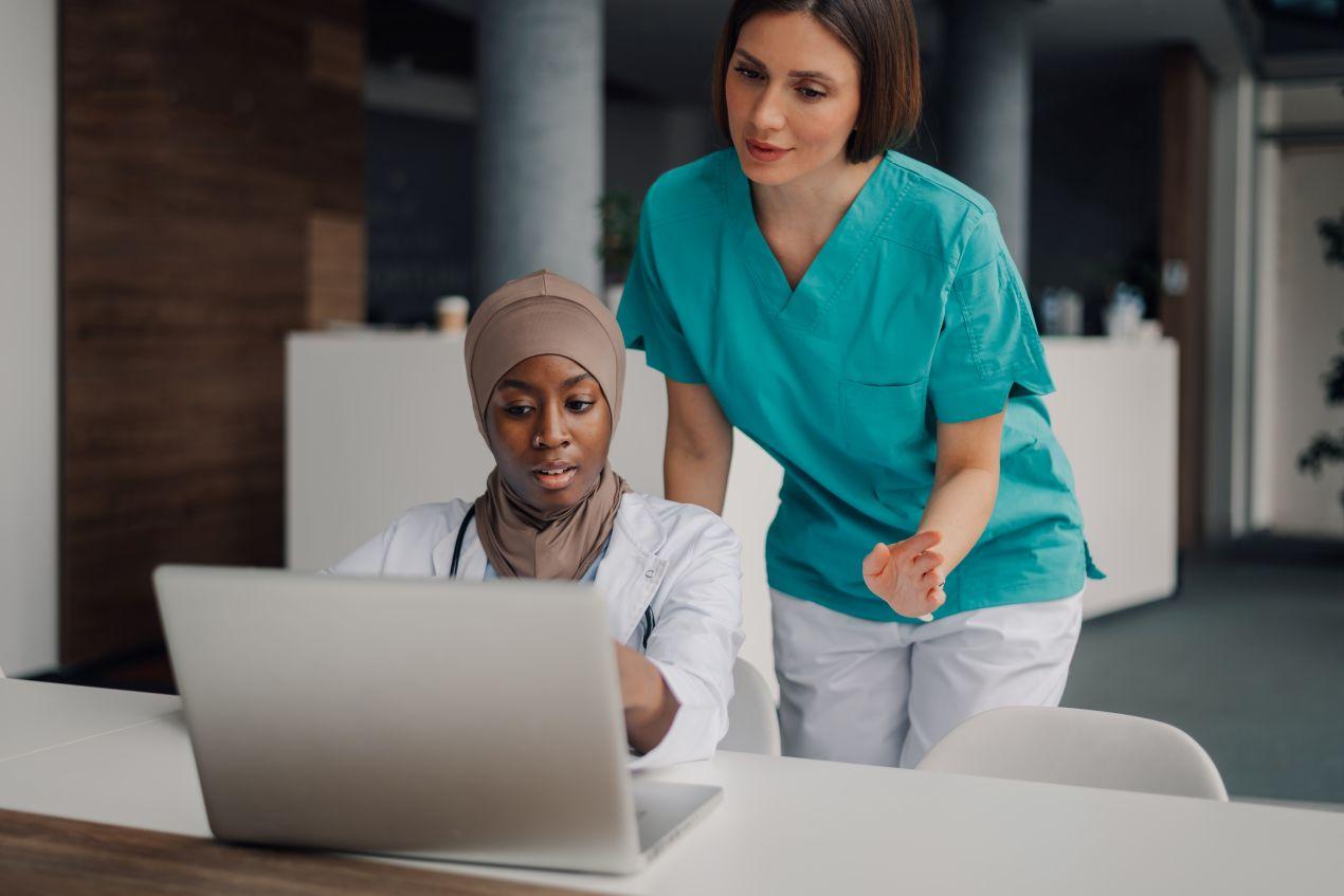 E-Learning Hygiene: Zwei Pflegekraefte lernen gemeinsam am Laptop und besprechen digitale Hygieneschulung