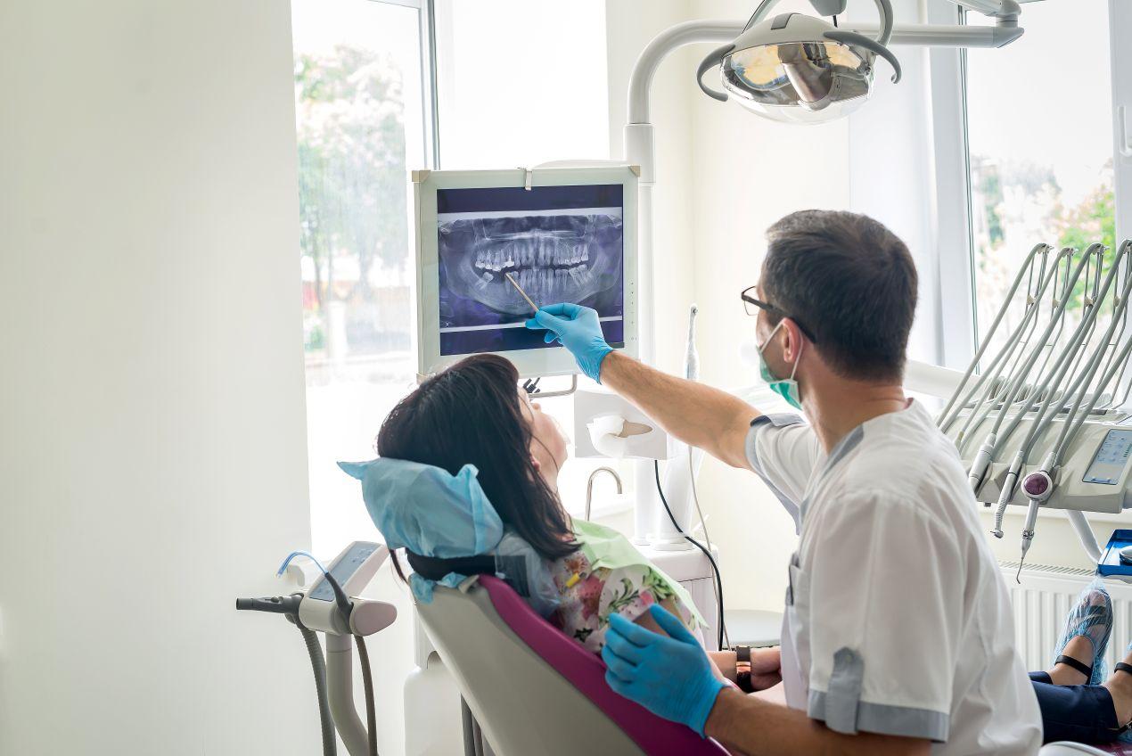 Zahnarzt zeigt Patientin ein digitales Roentgenbild auf dem Bildschirm, moderne Technik beim zahnarzt essen