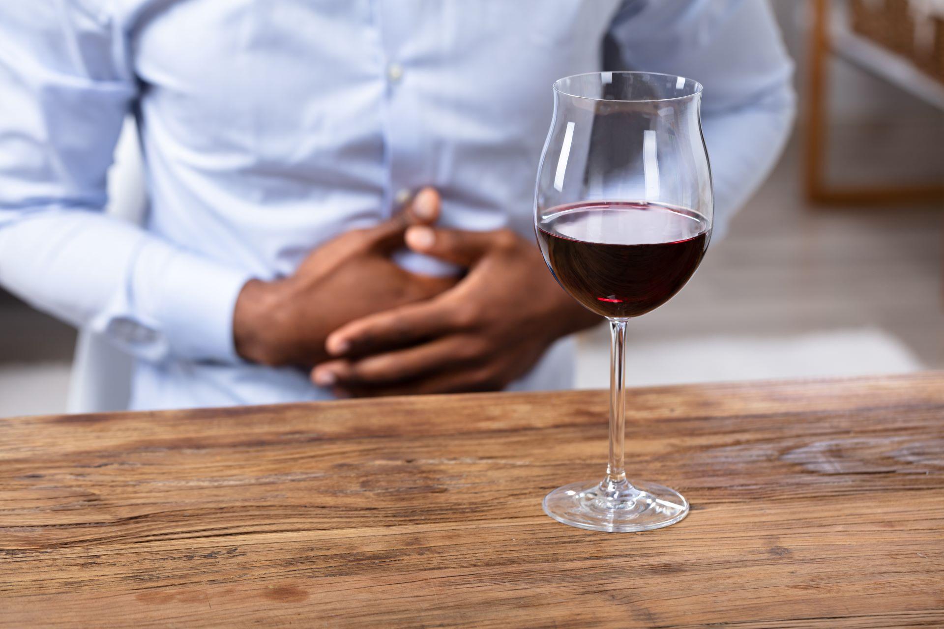 Person mit Bauchschmerzen vor Glas Rotwein