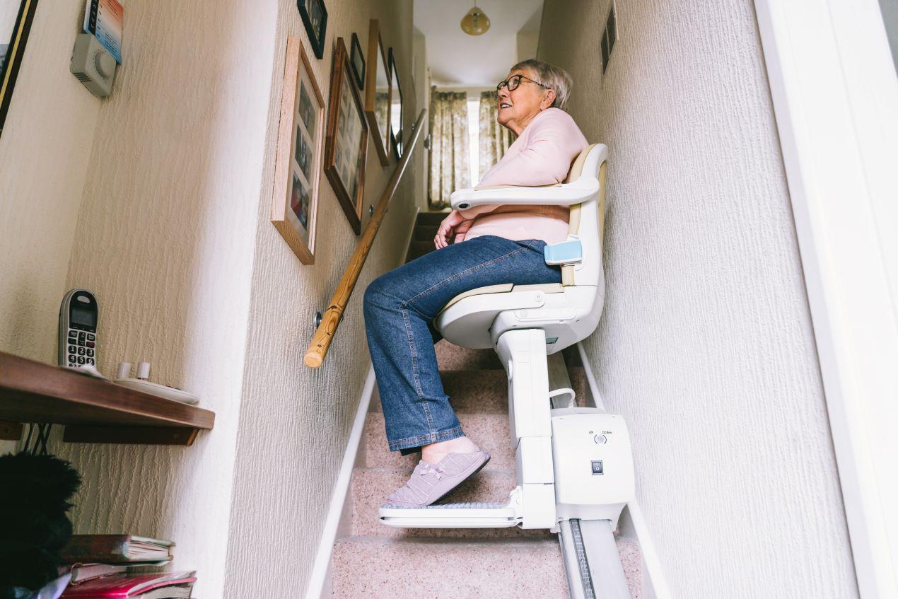 Aeltere Frau nutzt Treppenlift mit Plattform-Alternative als Sitzlift in einem schmalen Treppenhaus