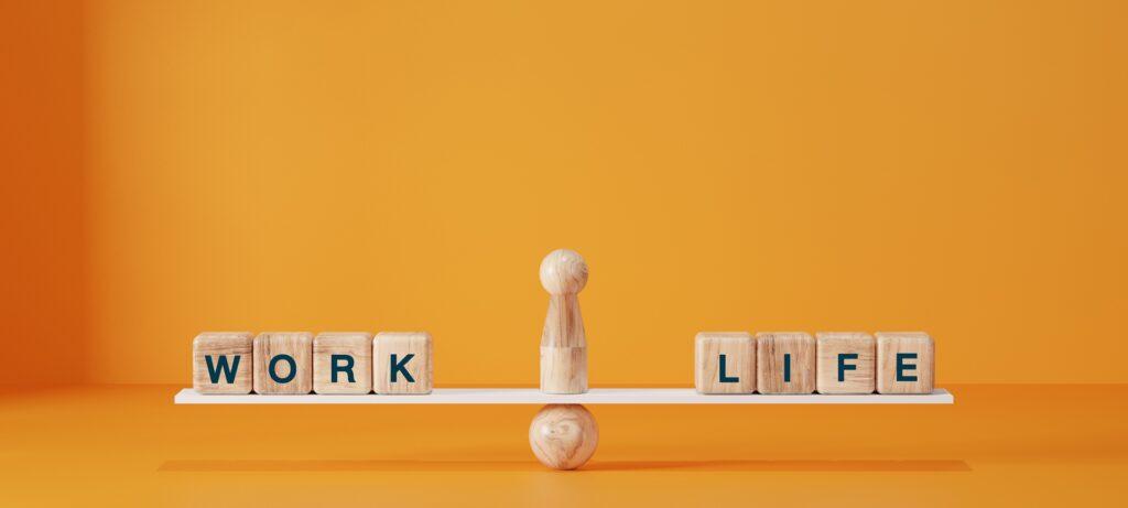 Holzbuchstaben Work Life auf Waage vor orangefarbenem Hintergrund | mobiler Arbeitsplatz